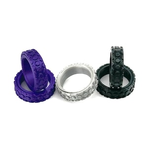 May include: Three silicone fidget rings in purple, silver, and black. Each ring has a textured surface with raised bumps.