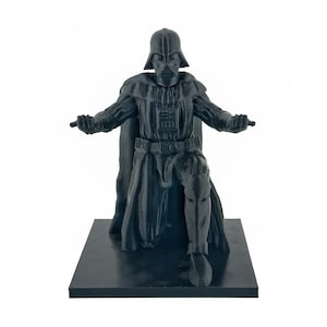 May include: A black plastic figurine of Darth Vader kneeling on a black base. The figurine is detailed with a black cape and a black helmet with a red visor.