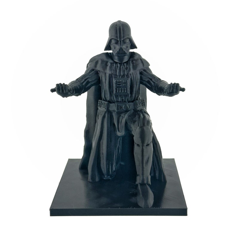 May include: A black plastic figurine of Darth Vader kneeling on a black base. The figurine is detailed with a black cape and a black helmet with a red visor.