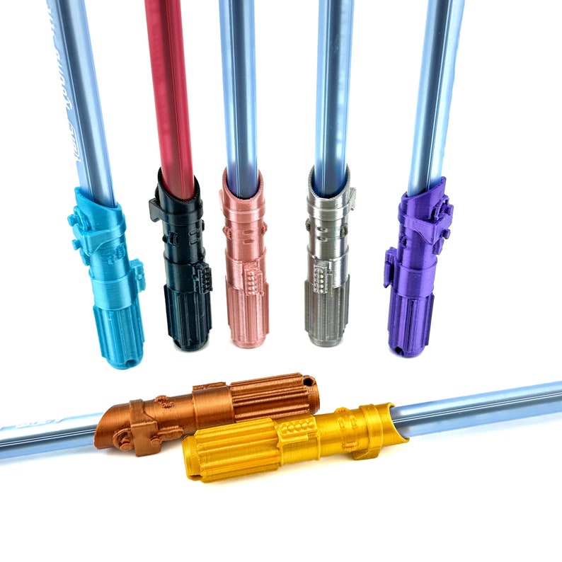 May include: Five lightsaber pens in different colors: blue, red, rose gold, silver, and purple. The pens are all in focus and are arranged in a row. There are two additional lightsaber pens in gold and copper colors, lying on a white surface.