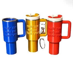 Könnte beinhalten: Drei Reisebecher mit Deckel und Henkeln. Die Becher sind blau, gold und rot. Jeder Becher hat den Text "Möge die 4. mit dir sein" aufgedruckt.