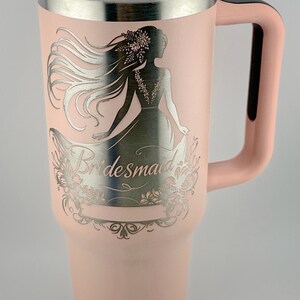 May include: A pink stainless steel tumbler with a silver design of a woman in a dress and the word "bridesmaid".