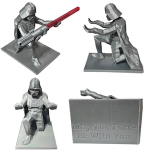 May include: Three gray 3D printed figurines of Darth Vader from Star Wars. The first figurine shows Darth Vader holding a red lightsaber. The second figurine shows Darth Vader kneeling with his arms outstretched. The third figurine shows Darth Vader kneeling with his arms outstretched and a gray plaque with the text "May The Force Be With You".