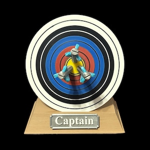 May include: A wooden base with a target and three arrows sticking out of it. The target has a red, blue, and black bullseye. The base has the word "Captain" written on it.