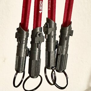 May include: Four gray lightsaber keychains with red pencils attached. Each keychain has a silver ring.