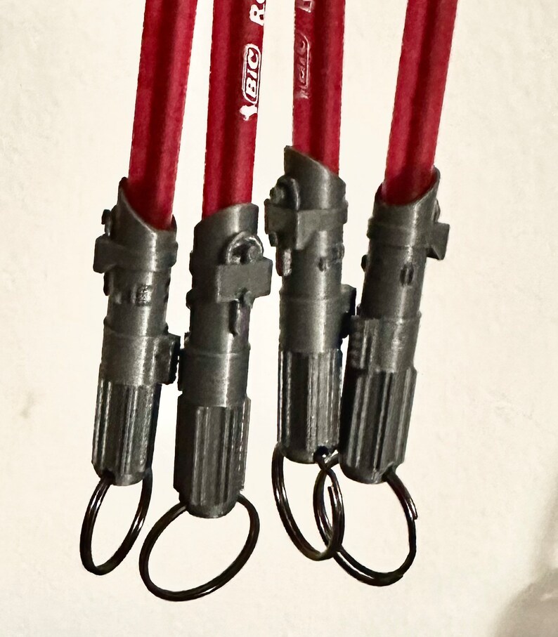 May include: Four gray lightsaber keychains with red pencils attached. Each keychain has a silver ring.