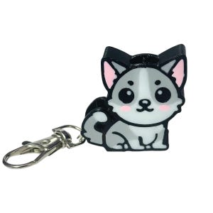Könnte beinhalten: Ein Schlüsselanhänger im Cartoon-Stil mit einem Husky-Hund-Design. Der Anhänger hat einen silbernen Verschluss und einen dreidimensionalen Husky mit schwarzen, grauen und weißen Farben, rosa Ohren und rosigen Wangen.