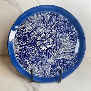 May include: A blue and white ceramic plate with a floral design. The plate has a blue rim and a white center with a floral pattern in blue.
