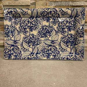 May include: Rectangular serving platter with a cream-colored base and a blue floral hydrangea pattern. The platter has a slightly raised edge and is suitable for serving food. The floral design is detailed and covers the entire surface.