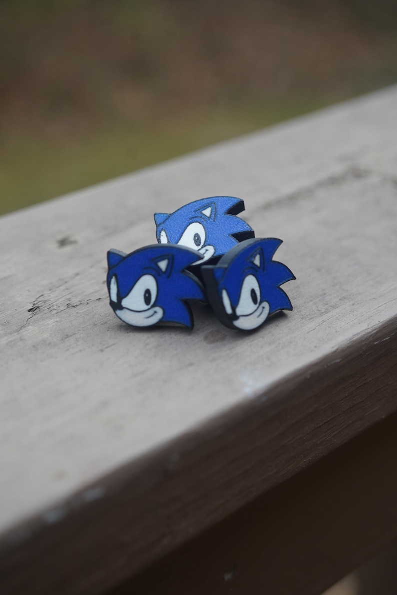 May include: Three blue and black 3D printed Sonic the Hedgehog figurines. The figurines are facing different directions and are arranged in a triangular shape.