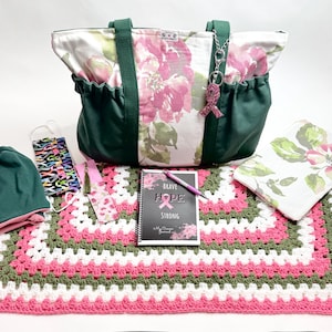 May include: A collection of items including a tote bag, beanie, face masks, bookmark, journal, and a crocheted blanket. The tote bag features a floral pattern with green accents. The journal has the text "Brave Hope Strong". The blanket is pink, white, and green.