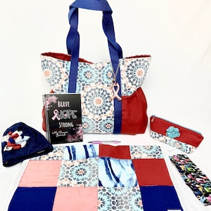 May include: A blue and white patterned tote bag with a red accent, a journal with the words "Brave Hope Strong" on the cover, a blue and white patterned quilt, a blue and white patterned hat, a blue and white patterned pencil case, and a pink ribbon charm.
