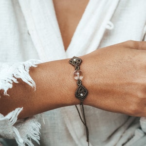 May include: A brown macrame bracelet with a clear crystal bead and a knotted closure.