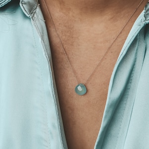 Puede incluir: Un delicado collar de cadena de plata con un colgante de piedra preciosa azul claro. El colgante tiene forma de lágrima y un acabado liso y pulido.