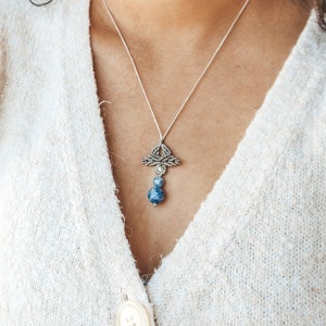 May include: A silver necklace with a blue gemstone pendant. The pendant is a geometric design with a small blue stone in the centre.