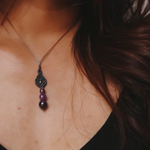 Può includere: Una collana d'argento con un ciondolo in macramè nero e tre perle di pietre preziose viola.