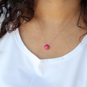 May include: A delicate necklace with a single, faceted, pink gemstone pendant.
