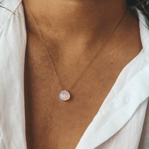May include: A delicate gold chain necklace with a single, round, iridescent opal pendant.