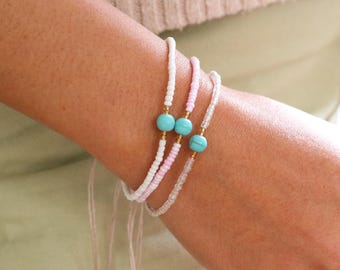 May include: Three beaded bracelets in white, pink, and clear with turquoise and gold accents. The bracelets are strung on a pink cord with adjustable closures. The bracelets are worn on a wrist.
