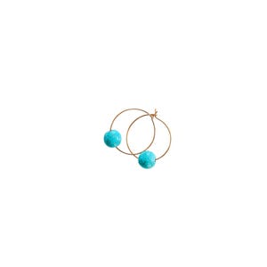 May include: A pair of gold hoop earrings, each featuring a vibrant turquoise bead. The earrings are displayed against a plain white background, highlighting their simple elegance and color contrast.