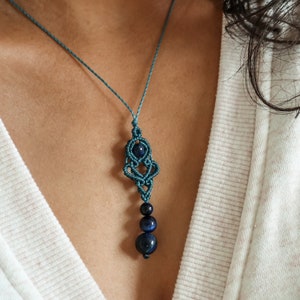 May include: A teal blue macrame necklace with a dark blue gemstone pendant and three dark blue beads.