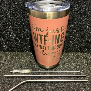 May include: A coral-colored stainless steel tumbler with a clear lid and a gold rim. The tumbler has the phrase "I'm just WTF-ing my way through life" etched on the front. Includes two stainless steel straws and a cleaning brush.