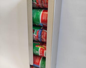 Puede incluir: Un dispensador de metal plateado que contiene varias latas de productos de tomate. Las latas son rojas y verdes con texto en italiano. El dispensador está diseñado para contener las latas en una fila vertical.