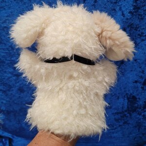 Pu&ograve; includere: Burattino di cane di peluche bianco con occhi neri e un collare di feltro nero. Il burattino &egrave; su una mano.