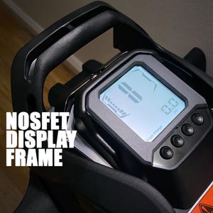 Peut inclure: Un cadre d'affichage numérique noir et gris avec le texte "NOSFET DISPLAY FRAME". L'écran affiche un écran bleu avec des chiffres et un indicateur de batterie. Il y a trois boutons en dessous de l'écran et une étiquette d'avertissement.