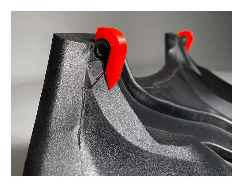 May include: Close-up of a black plastic object with two red plastic tabs. The object has a textured surface and appears to be part of a larger item.