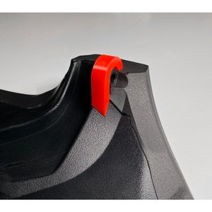 May include: Close-up of a black and gray plastic object with a red plastic tab. The tab is attached to the object with a small black screw.