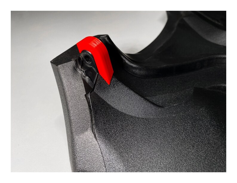 May include: Close-up of a black plastic object with a red plastic tab. The object has a textured surface and a sharp edge.