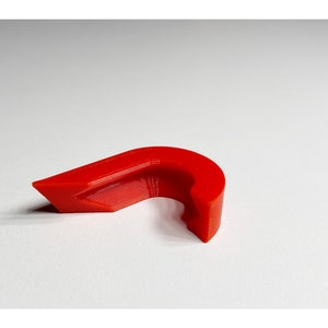 May include: A bright red plastic cable clip, designed to hold cables in place. The clip has a curved shape and a small opening for the cable to pass through.