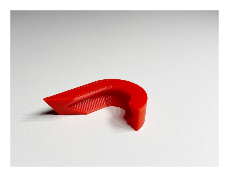 May include: A bright red plastic cable clip, designed to hold cables in place. The clip has a curved shape and a small opening for the cable to pass through.