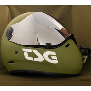Pu&ograve; includere: Un casco verde con una visiera argentata e la scritta "TSG" in lettere bianche sul lato.