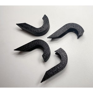 May include: Four black plastic hooks with a textured finish. The hooks are shaped like a curved letter 'C' and have a small lip on the top.