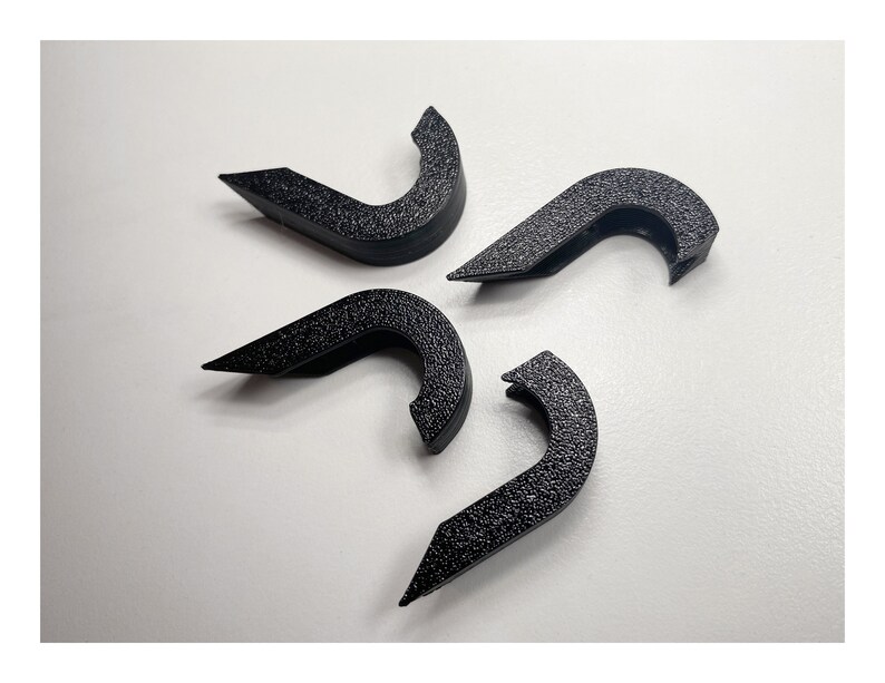 May include: Four black plastic hooks with a textured finish. The hooks are shaped like a curved letter 'C' and have a small lip on the top.