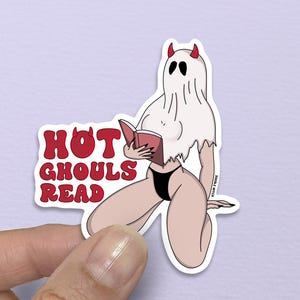 May include: A sticker featuring a cartoon ghost with red horns and a black bikini, reading a book. The text "HOT GHOULS READ" is in red letters. The ghost is white with black eyes.