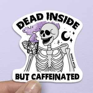 May include: A white sticker featuring a cartoon skeleton holding a coffee cup, with the text "DEAD INSIDE BUT CAFFEINATED". The skeleton has a smiling skull and is surrounded by purple smoke and celestial elements.