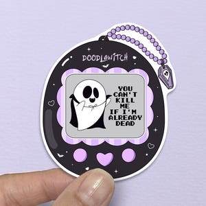 May include: A black and purple sticker in the shape of a vintage handheld game. The screen displays a ghost graphic with the text "YOU CAN'T KILL ME IF I'M ALREADY DEAD." The sticker has a beaded chain and a small charm.