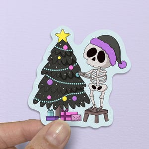 May include: A sticker featuring a cartoon skeleton wearing a Santa hat, decorating a Christmas tree. The tree is adorned with colorful ornaments and a star. Presents are at the base of the tree. The skeleton is standing on a small stool.