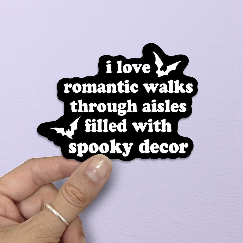 Puede incluir: Una pegatina negra troquelada con texto blanco que dice: "i love romantic walks through aisles filled with spooky decor". El dise&ntilde;o presenta dos siluetas de murci&eacute;lagos blancos, una situada en la parte superior derecha y otra en la inferior izquierda.