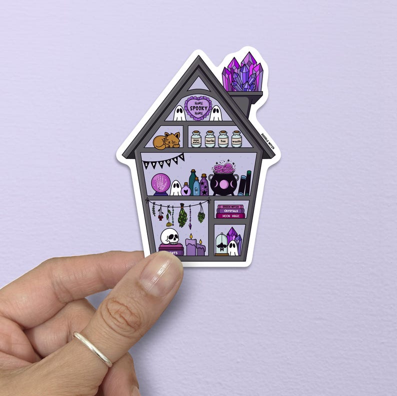 May include: A house-shaped sticker with a spooky theme. The house is filled with witchy items, including crystals, potions, a crystal ball, and ghosts. The text "Home Spooky Home" is visible on the top of the house.