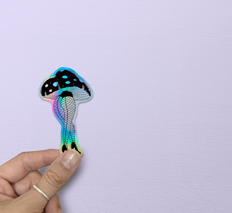 May include: A holographic sticker featuring a mushroom design. The mushroom cap is black with white spots, and the stem depicts legs in fishnet stockings and high heels. The sticker has a rainbow iridescent effect.