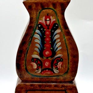 Puede incluir: Un reloj de madera con acabado marrón y diseños florales pintados a mano en rojo, azul y blanco. La esfera del reloj tiene números romanos. El reloj mide aproximadamente 30 cm de alto.