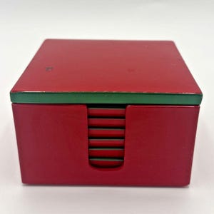 Puede incluir: Un juego de posavasos de madera rojo y verde con una pila de posavasos dentro de una caja roja.