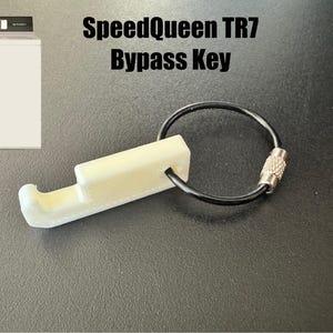 May include: A cream-coloured SpeedQueen TR7 Bypass Key attached to a black keyring with a silver clasp. The key has a rectangular body with a curved end. The text "SpeedQueen TR7 Bypass Key" is displayed above the key.