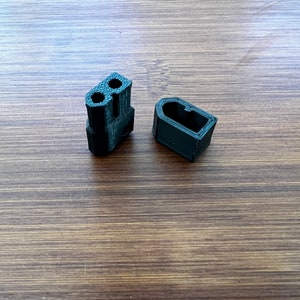 Peut inclure: Deux pièces en plastique noir, l'une avec trois trous et l'autre avec un seul trou, probablement pour une imprimante 3D.