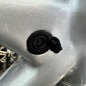 Può includere: Primo piano di un telaio di bicicletta argentato con una porta di ricarica nera. La porta ha un coperchio nero aperto, che rivela i pin di ricarica.