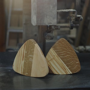 Könnte beinhalten: Zwei dreieckige Holz-Untersetzer mit einer hellbraunen und dunkelbraunen Holzmaserung. Die Untersetzer werden von einer Bandsäge geschnitten.